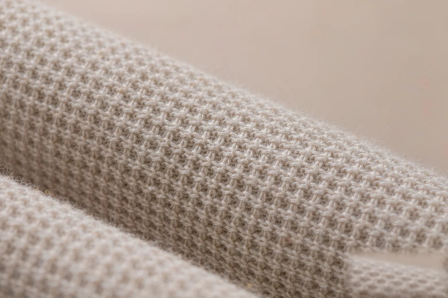Macro close-up of fine-gauge cotton and linen knit fabric in warm oat tone — breathable weave detail