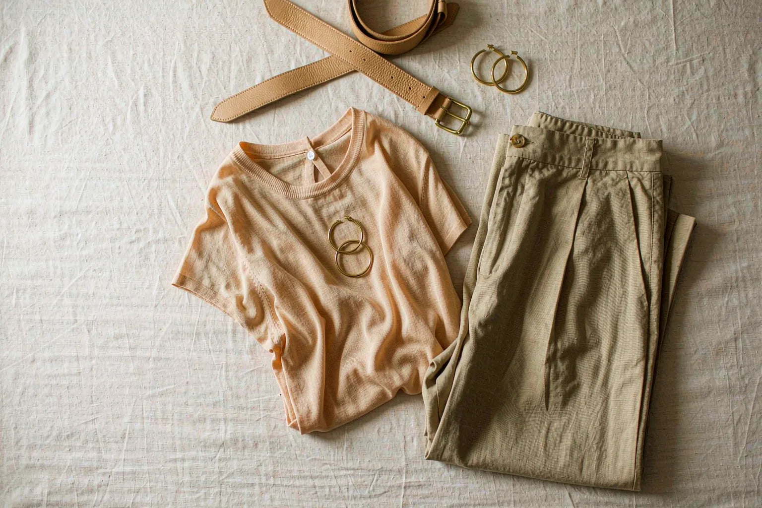 Tone-on-tone outfit flat lay pairing an apricot knit top with khaki wide-leg trousers and tan leather accessories in warm neutral tones