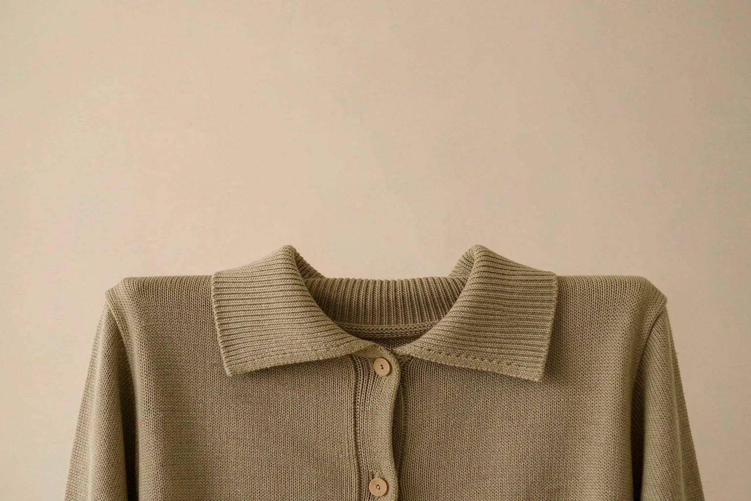 Macro detail of a clean fine-gauge knit cardigan in khaki showing even stitching and minimal hardware, with no visible logo