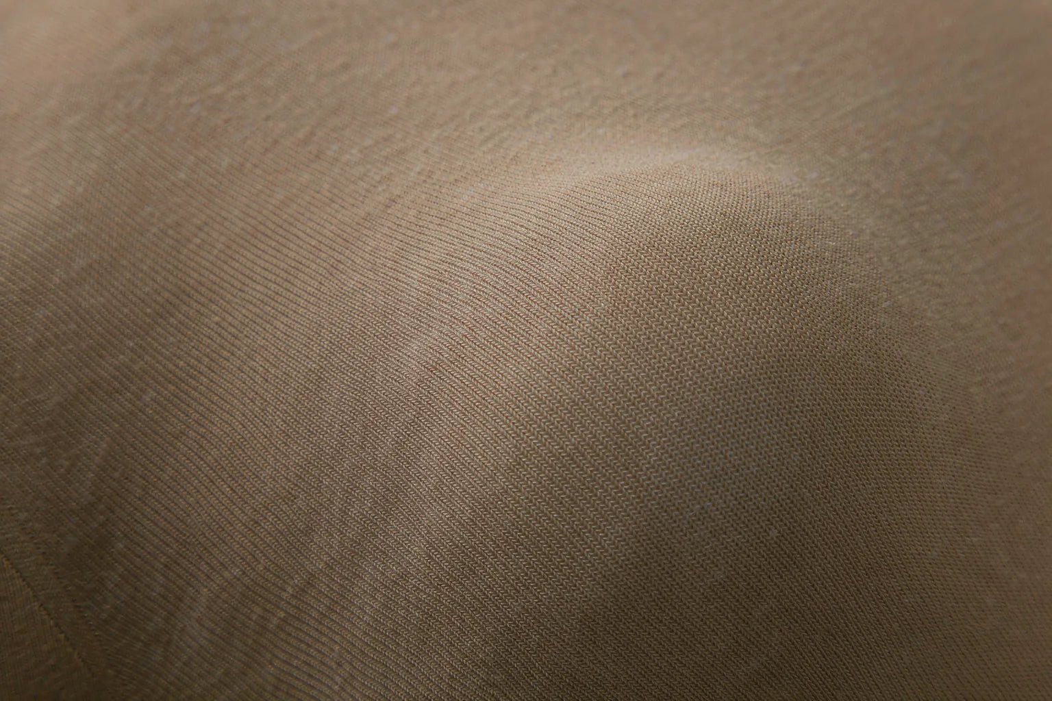 Extreme close-up of fine-gauge oatmeal seamless knit fabric with a smooth uninterrupted surface, on a warm cream background