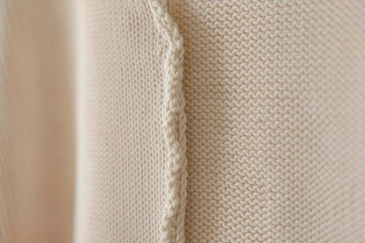 Close-up of the interior side seam of a cream knitted top, showing the stitched seam ridge on a plain off-white background